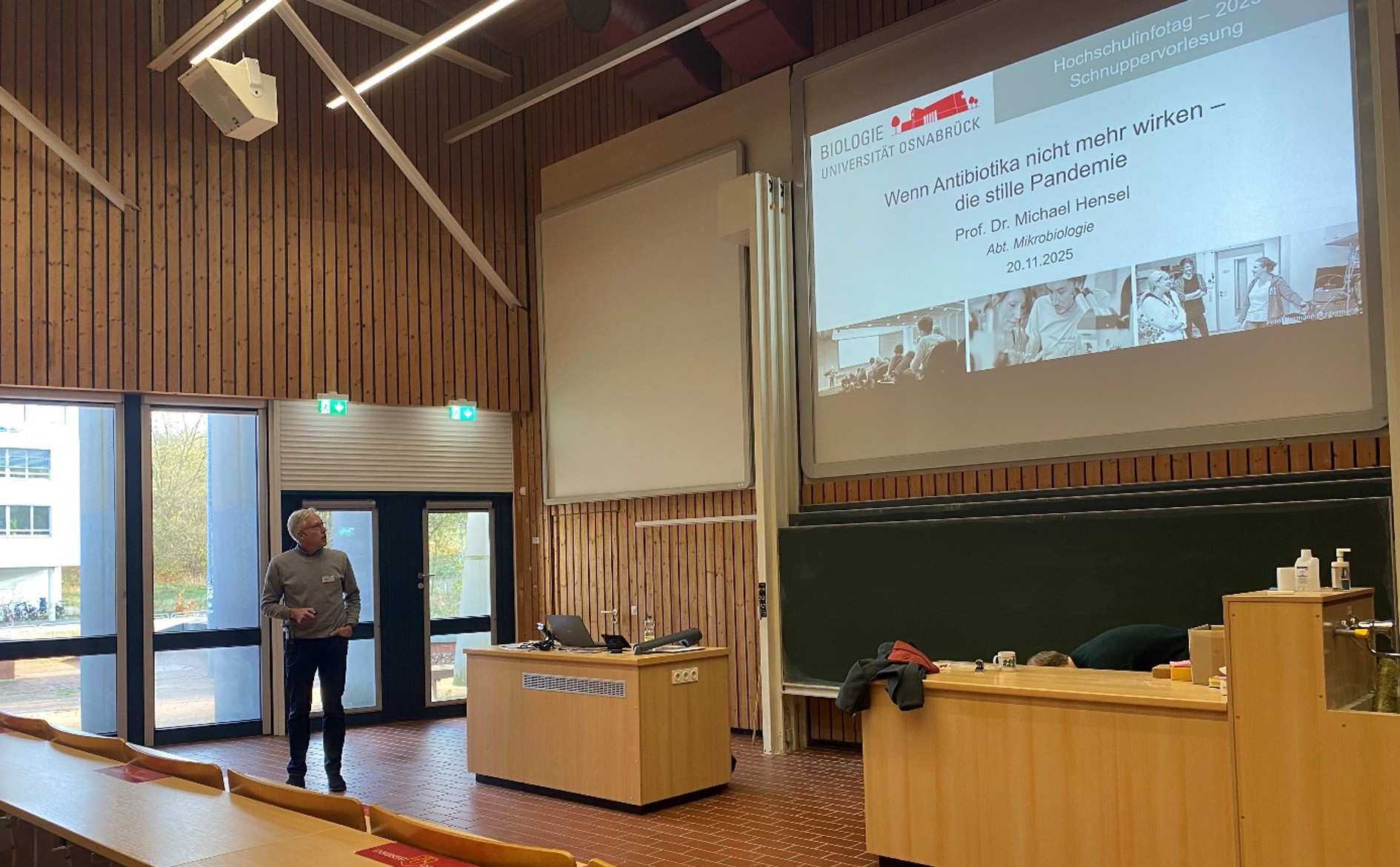 A man is standing in a lecture hall holding a pointer in his hand.