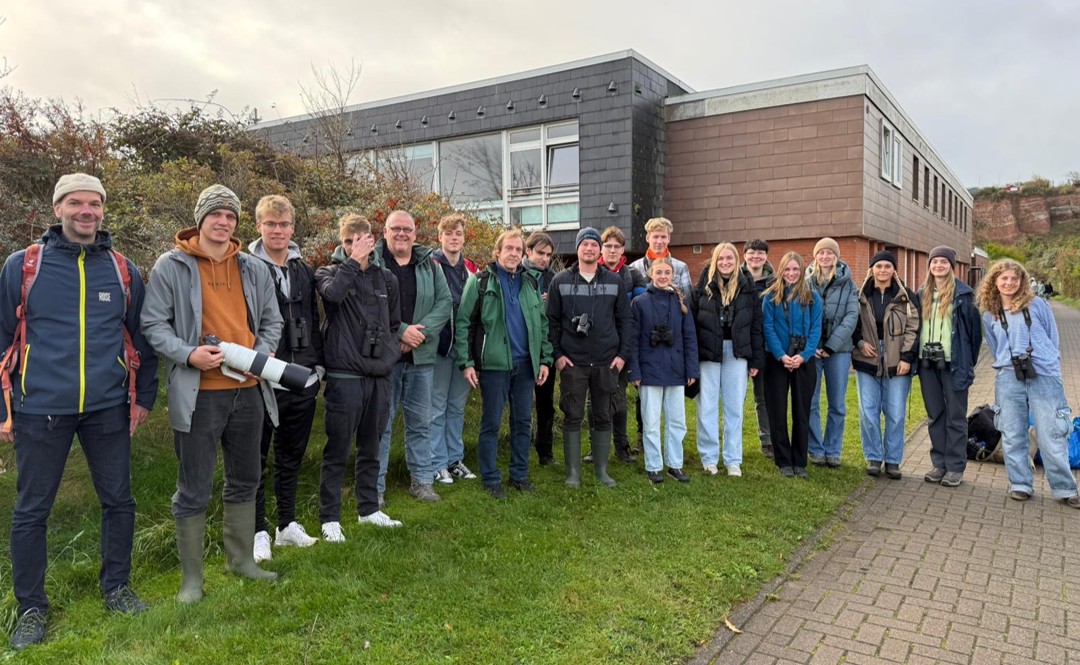 Rund zwanzig Personen stehen vor einem Gebäude, einige tragen Ferngläser.